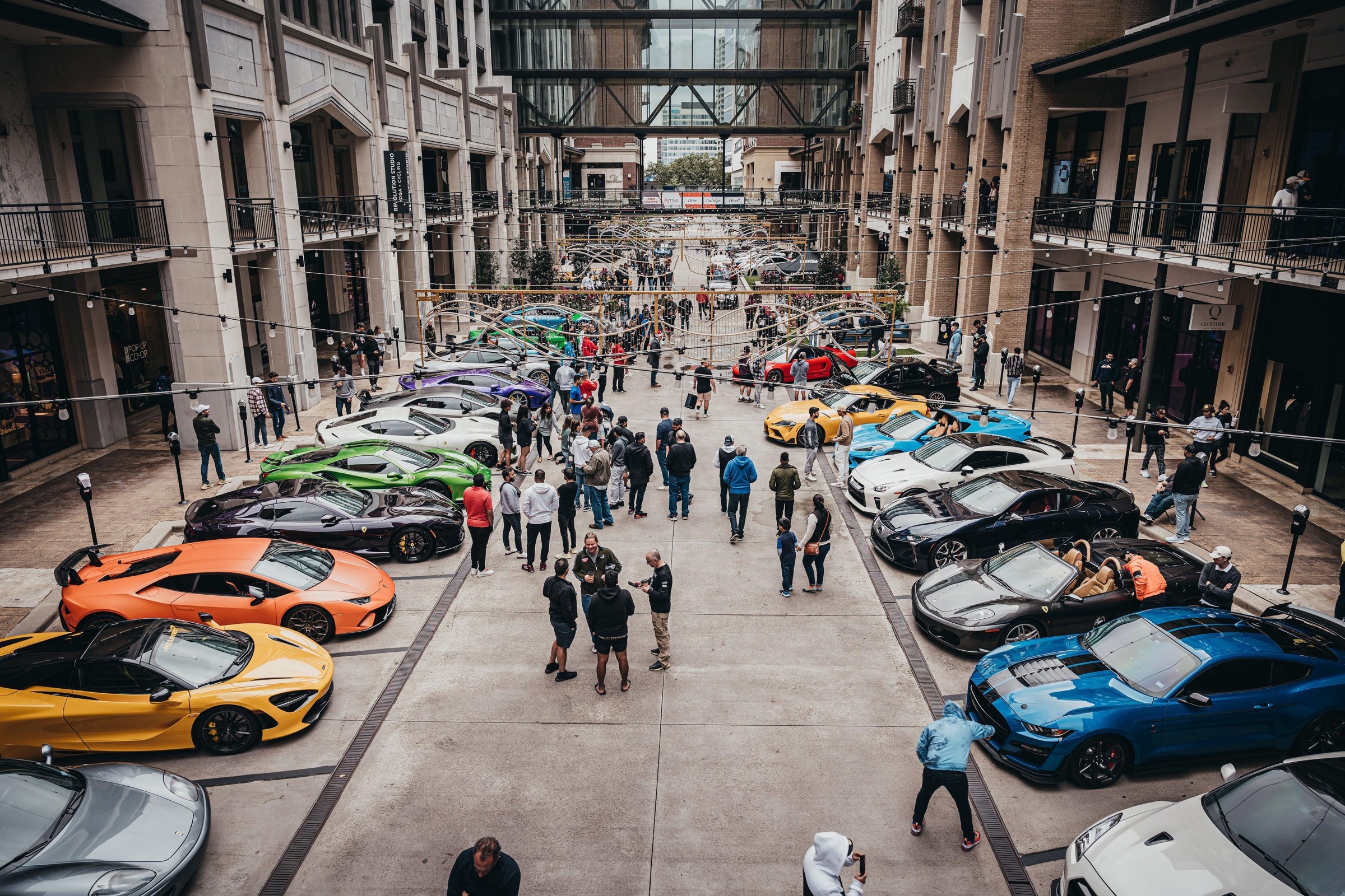 Aerial view of a supercar meet — Lamborghinis, McLarens, Ferraris in a city plaza